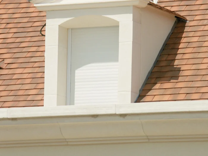 Corniche bandeau bouchardée sous une lucarne à fronton, toit de tuiles