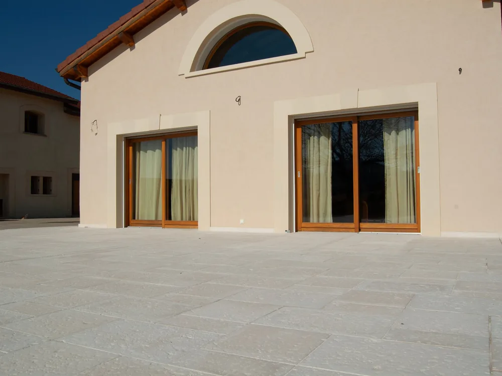 Grande terrasse en dalles bouchardées claires devant une façade aux baies vitrées