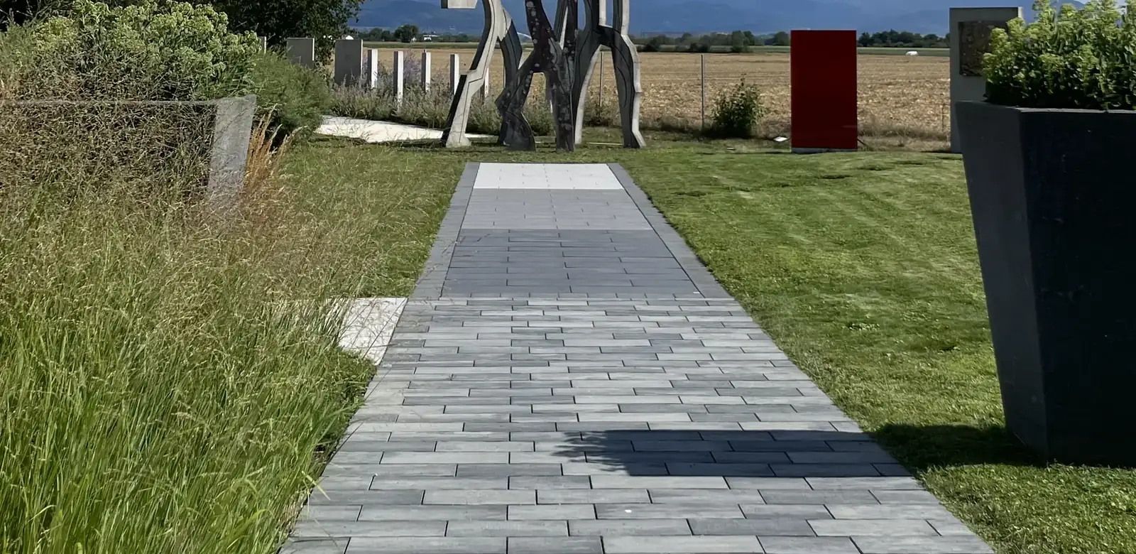 Allée pavée traversant un jardin vers une sculpture