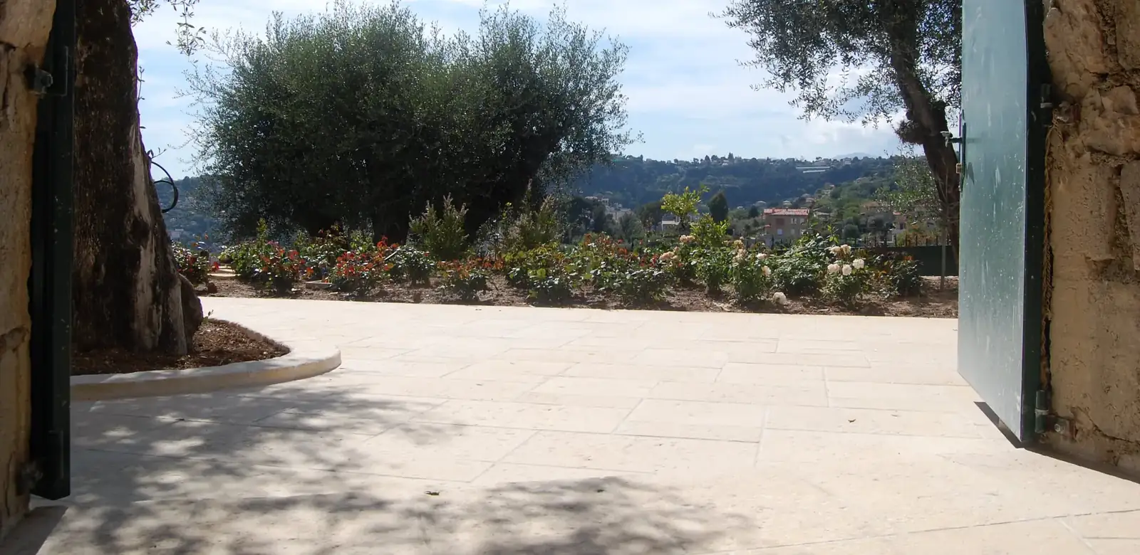 Terrasse en dalles bouchardées ocre ouverte sur un jardin d'oliviers